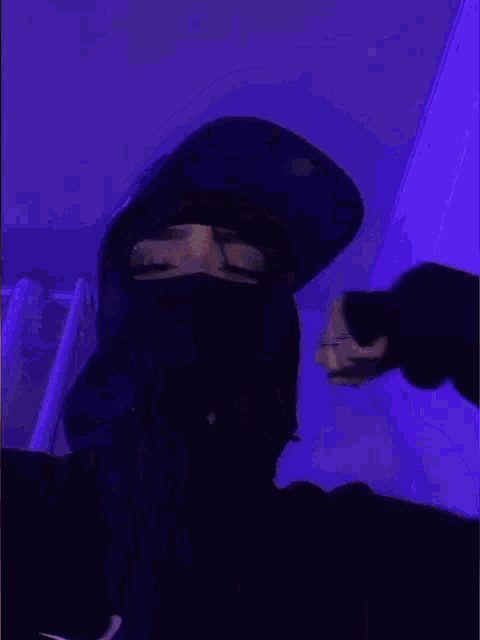 a person wearing a mask and a baseball cap is standing in front of a purple wall .