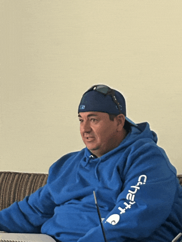 a man wearing a blue carhartt hoodie sitting on a couch