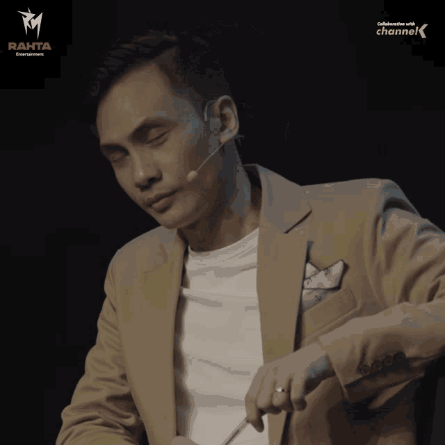 a man with a microphone in his ear is sitting in front of a sign that says channel k