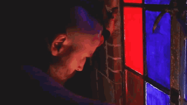 a man is looking through a stained glass window in a dark room