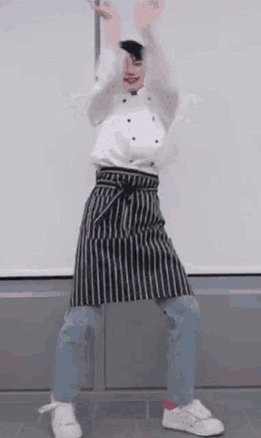 a man wearing an apron and a chef 's uniform is making a heart shape with his hands .