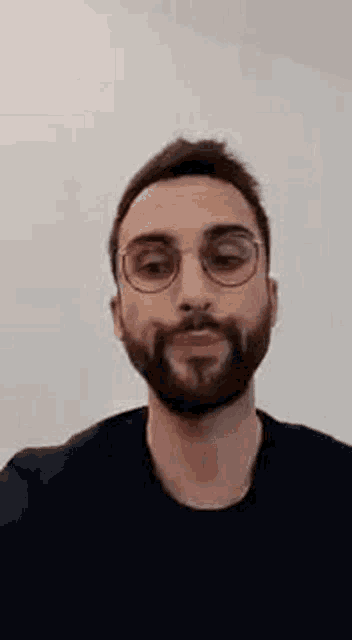 a man with a beard is wearing glasses and a black shirt .
