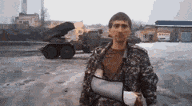 a man with a broken arm is standing in front of a military vehicle
