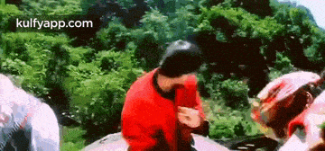 a man in a red sweater is sitting on a rock in the woods .