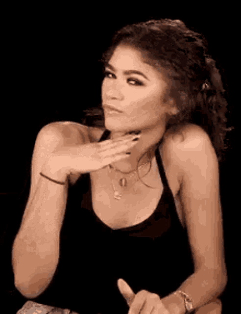 a woman in a black tank top is sitting down with her hand on her chin .