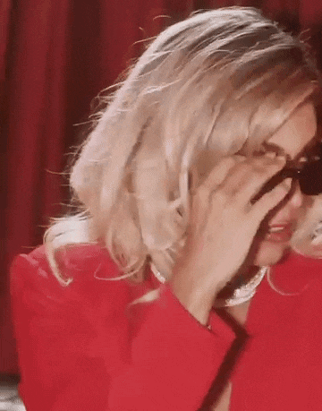 a woman wearing sunglasses and a red jacket is covering her face .
