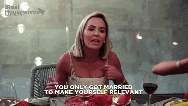 a woman is sitting at a table with a glass of wine and a sign that says real housewives