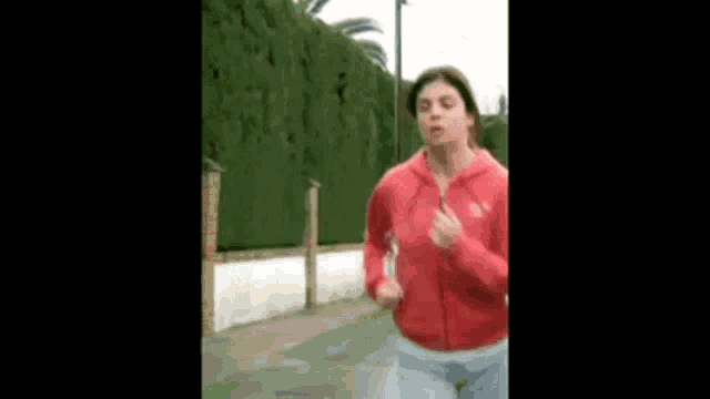 a woman in a red hoodie is jogging on a sidewalk .