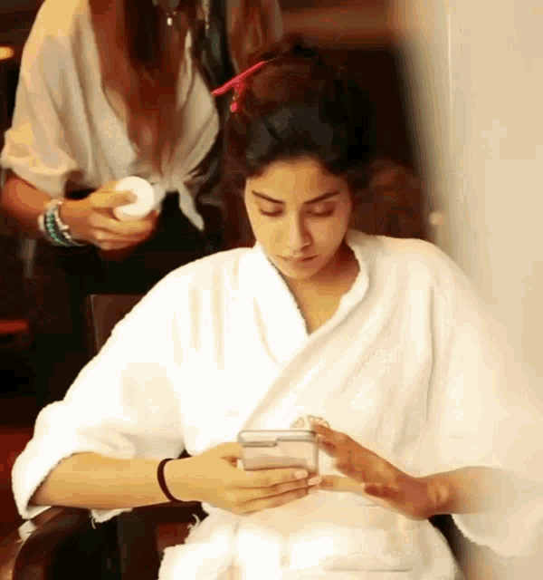 a woman in a bathrobe is looking at her cell phone