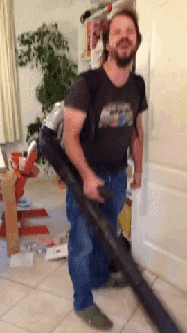 a man wearing a star wars shirt is holding a large vacuum cleaner