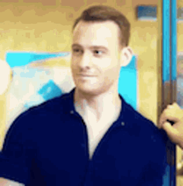 a man in a blue shirt is standing in front of a yellow wall and smiling .
