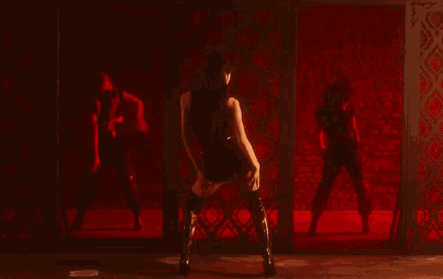 a woman in a black tank top is dancing in a dark room with a red background .