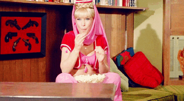 a woman in a pink and red outfit is sitting on a couch eating popcorn ..