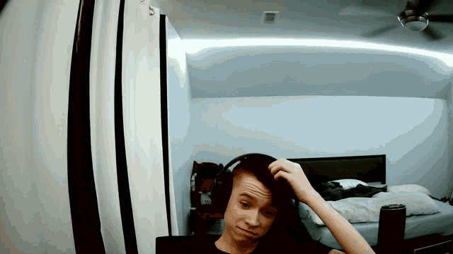 a young man wearing headphones scratches his head