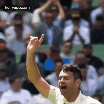 a man is raising his hand in the air in front of a crowd while playing tennis .