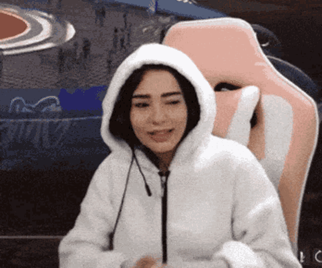 a woman is wearing a white hoodie and sitting in a pink chair