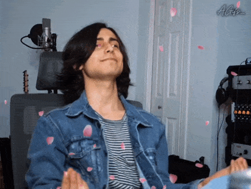 a man in a denim jacket is sitting in front of a microphone with petals falling from the ceiling