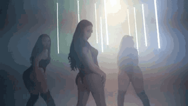 three women are dancing in a dark room with smoke coming out of the ceiling .