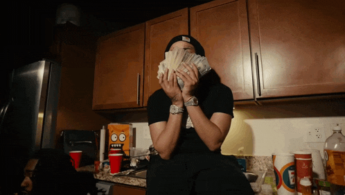 a man covering his face with a stack of money in a kitchen