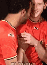 a man is kissing another man on the cheek while wearing a red shirt .