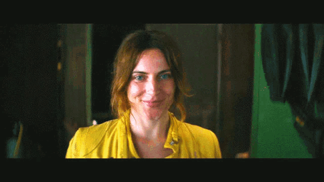 a woman wearing a yellow shirt is smiling in a dark room