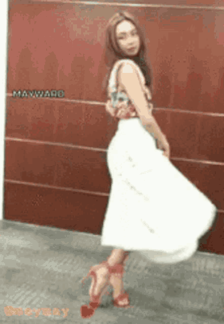 a woman in a white skirt and red heels is standing in front of a wall that says mayward