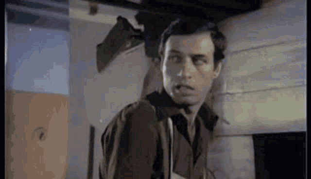 a man in a brown jacket is standing in a room with a broken window .