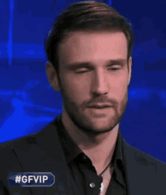 a man with a beard is wearing a suit and a black shirt and is looking at the camera .
