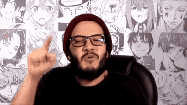 a man with glasses and a beard is sitting in front of a wall of anime characters .