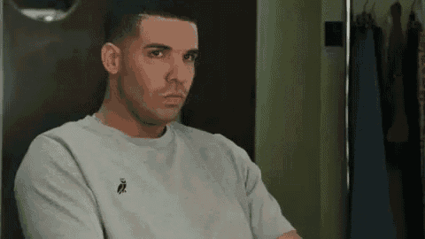 a man in a grey t-shirt is sitting in front of a mirror and making a funny face .