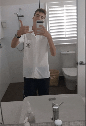 a young man taking a selfie in a bathroom with a shirt that says ' kingsford ' on it