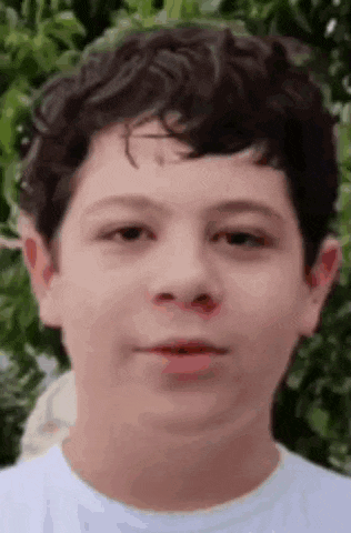 a young boy with curly hair is wearing a white shirt and making a funny face .