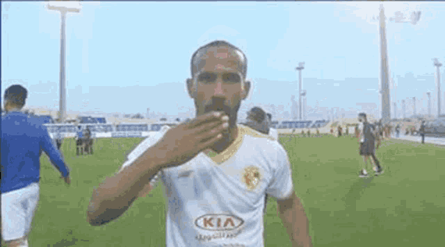 a soccer player wearing a kia jersey is blowing a kiss on the field .