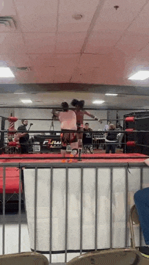 a couple of people are standing in a boxing ring and fighting each other .