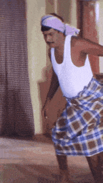 a man in a white tank top and plaid skirt is dancing .