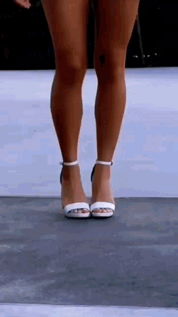 a woman wearing a pair of white heels is standing on a concrete surface .