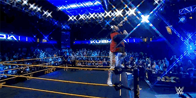 a wrestler in a red vest is jumping in the air in a wrestling ring