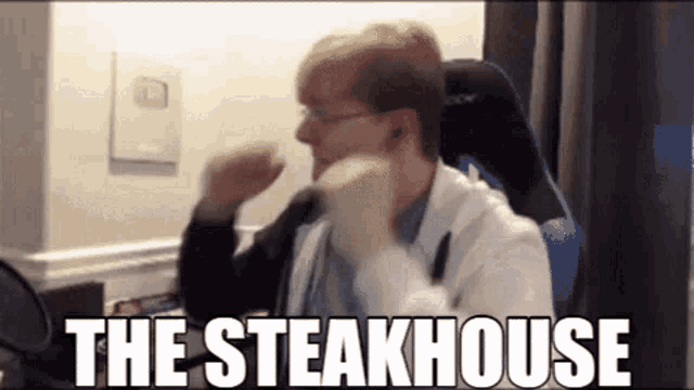 a man in a white coat and glasses is sitting in a chair with the words `` the steakhouse '' above him .