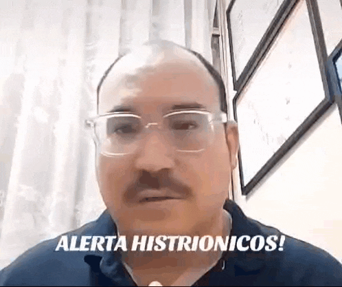 a bald man with glasses and a mustache is talking on a video call while wearing a blue shirt .