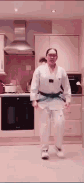 a woman in a karate uniform is standing in a kitchen .