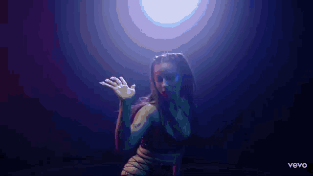 a woman in a black bra is dancing in a dark room with a blue light behind her .
