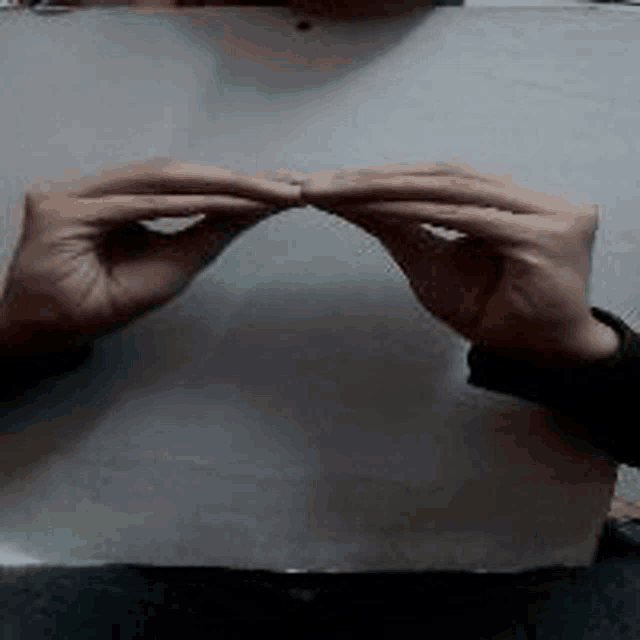 a person is holding a piece of paper in their hands and making a heart shape .