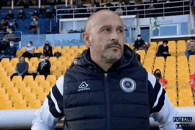 a man wearing an acerbis jacket stands in front of empty stadium seats