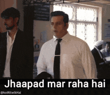 a man in a suit and tie is standing in front of a sign that says jhaapad mar raha hai on it