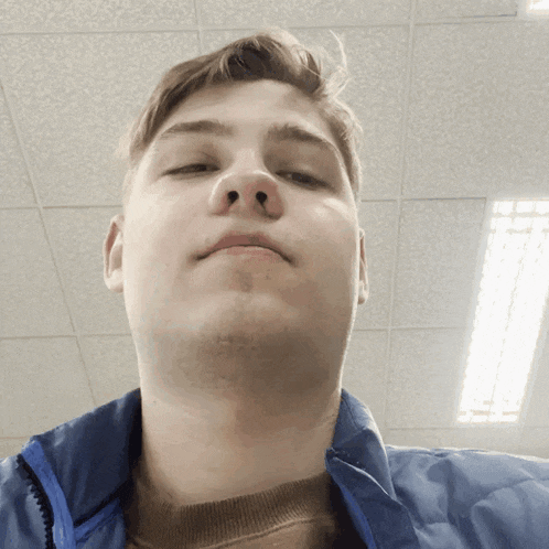 a young man in a blue jacket looks at the camera with his eyes closed