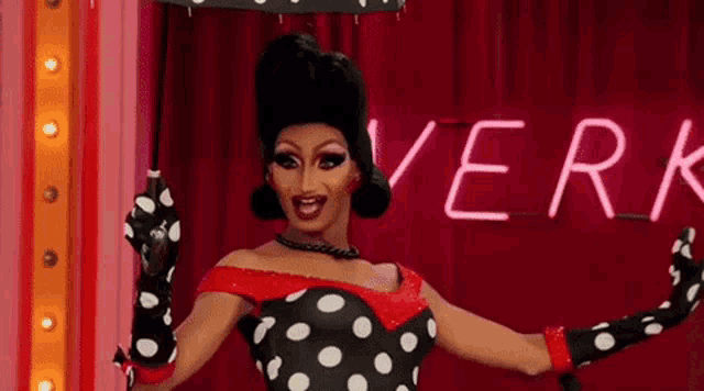 a drag queen is holding an umbrella in front of a neon sign that says " verk "