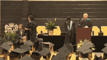 a man stands at a podium giving a speech at a graduation