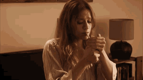 a woman is lighting a cigarette in a room with a lamp in the background