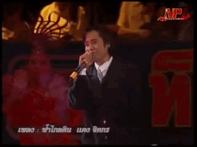 a man in a suit singing into a microphone with np written on the bottom right