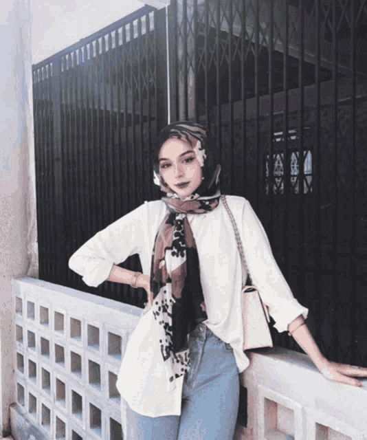 a woman wearing a scarf and a white shirt stands in front of a fence